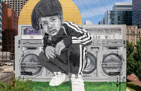 A young Black boy, in an Adidas track suit poses in front of a boom box.