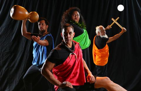 In front of a black curtain, four folks in different colored satin sashes pose. Two pose with their drum or drumsticks.