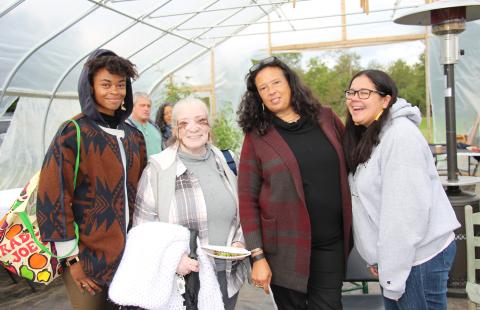 Artist Nia Holly (Nipmuc), Gail Rokotuibau (Narragansett/Pequot), Dawn Spears (Narragansett/Choctaw), and Samantha Fry (Narragansett) stand together and smile facing the camera inside a high tunnel at the Markets & Marketing workshop