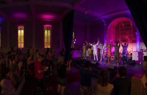 Panomrama of an audience and a band taking a bow on a stage.