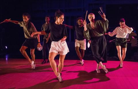 On a stage with a pink floor, six folks dance in casual outfits.