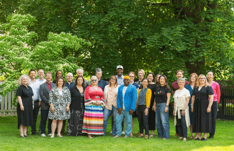 Outside, a large group of smiling folks in a mix of muted and vibrant outfits.