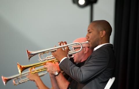 On an outdoor stage, three men play brass instruments.