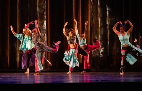 On a stage, five dancers wear color costumes.