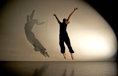 A spotlit figure jumps with arms outstretched. Their shadow is left of them in sharp focus.
