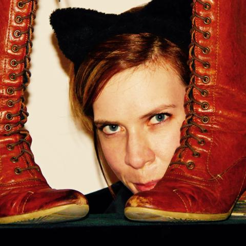A woman in cat ears peaks around a pair of boots.