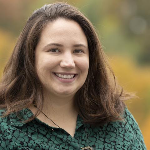 Woman outside smiles in front of autumnal trees