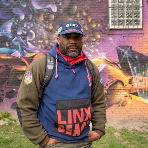 In front of a galaxy mural on the side of a brick building, Rob wears a cap and a hoodie.