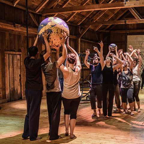 In a barn-like building, a group of people roll balls that look like earth. Another person walks on a wheel.