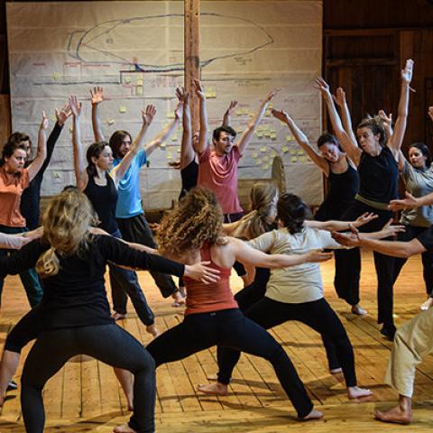 A group of folks dance in a circle with their arms raised.