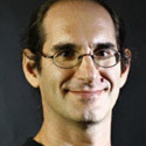 Neal smiles in a black shirt in front of a black background