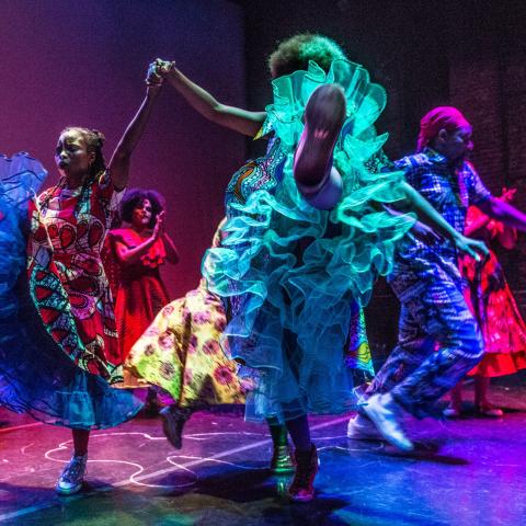 Six folks of color, in neon gowns, dance in spotlights.