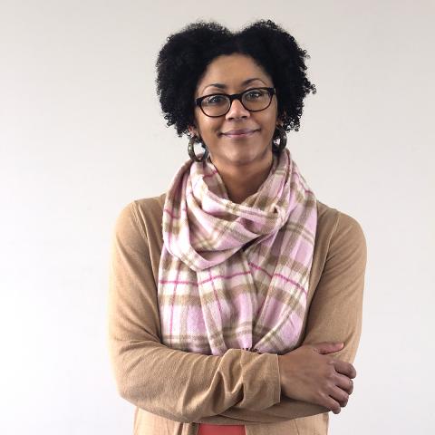Ashleigh crosses her arms and smiles in front of a gray wall.
