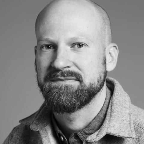 A black and white photo of a man with a beard and a shaved head.