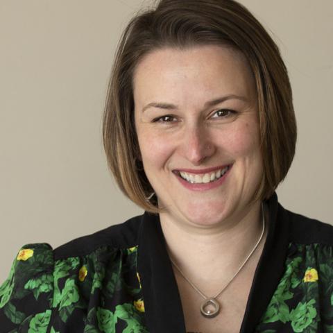 A woman with brown bobbed hair wears a black and green jacket with yellow flowers