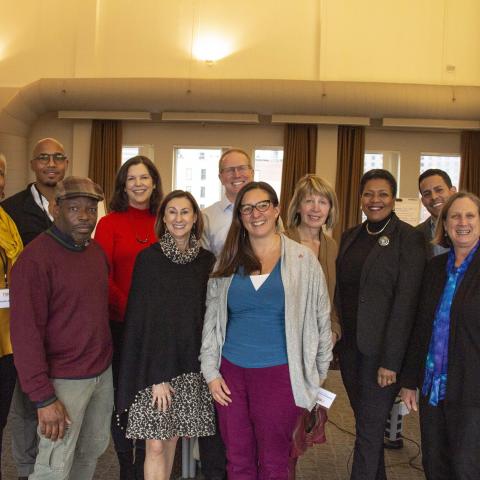 Eleven adults in a conference room pose standing in two rows.