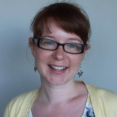 Woman in glasses and a yellow cardigan smiles.