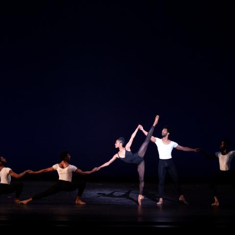 On a stage, dancers performer ballet in black and white unitards. 