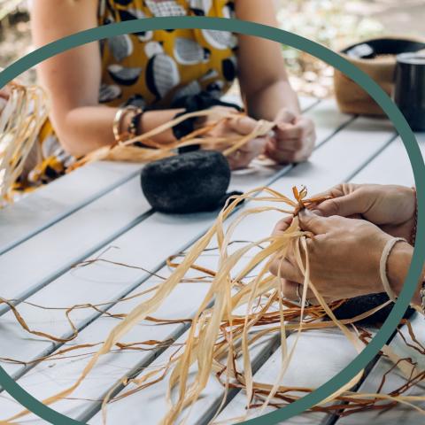 A green outline of a sphere overlaid on light-skinned women weaving hay at a picnic table.