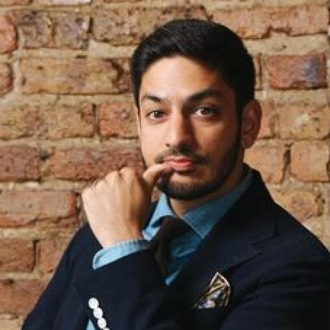 Asad sits in a brick room with his hand next to his chin