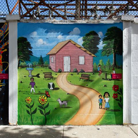 A mural, between two others, of a house with folks in the yard and sunflowers.