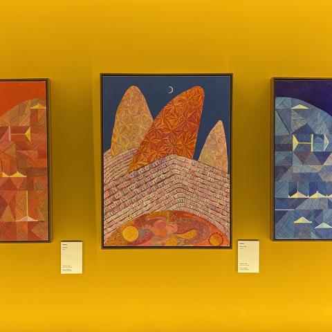 Three paintings: one red sky with the sun, one blue sky with rocks, and one night sky with water.