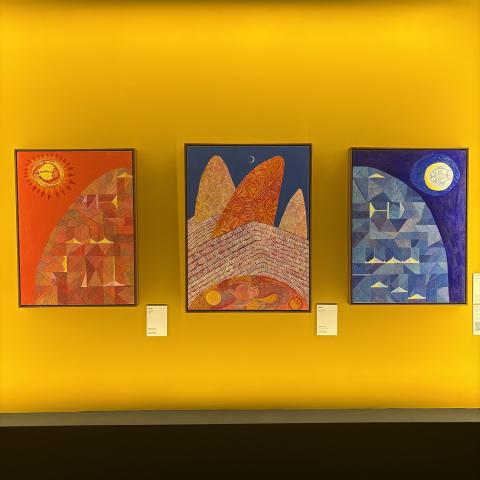Three paintings: one red sky with the sun, one blue sky with rocks, and one night sky with water.