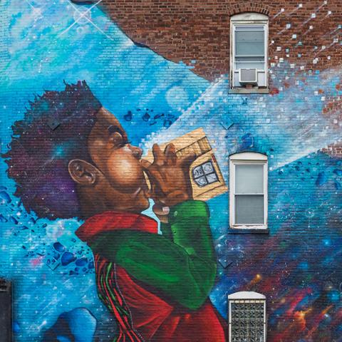 Mural of a little Black boy blowing into a video game cartridge and stars coming out of the other side.