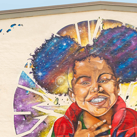 a colorful mural on the side of a building featuring a young black girl smiling 