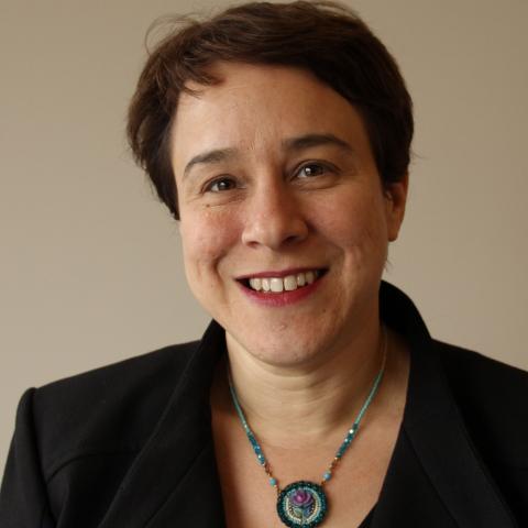 A woman with short hair and a beaded necklace wearing a black jacket