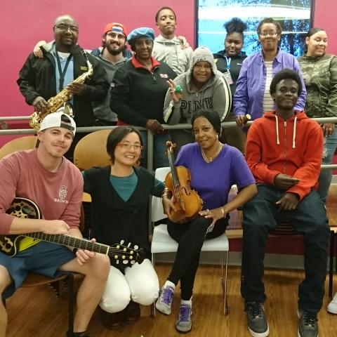 A musician poses with student musicians, some sitting and others leaning on a bannister