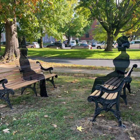 In a park, two benches face each other. A 3D photoshop of the eventual silhouettes seated on the benches are there in place of where they now sit.