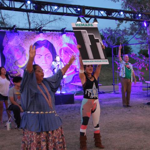 People hold signs up as if in protest, in front of a screen with a woman's face.