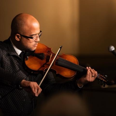 In a spotlight and a checkered jacket, Daniel plays the violin.