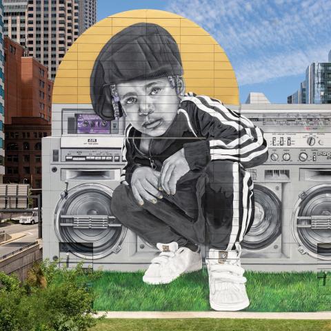 A young Black boy, in an Adidas track suit poses in front of a boom box.