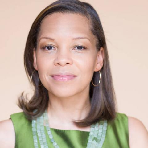 A woman with shoulder length hair, hoop earrings, and a beaded necklace over a green top.