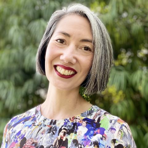 A cis woman who is half Japanese and half white. She has a grey bob and is wearing a multi-colored dress.