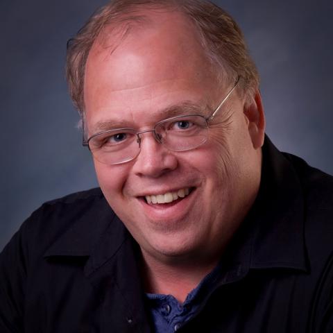 A white man with wire glasses and short light hair wearing a black shirt