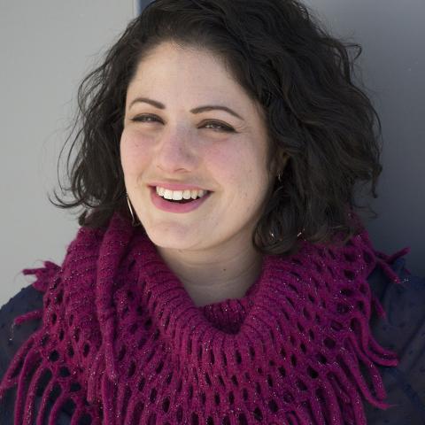 Denise smiles in a scarf in front of a blue wall
