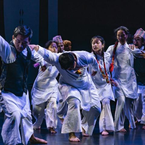 A group of performers dressed in white dance together on a stage.