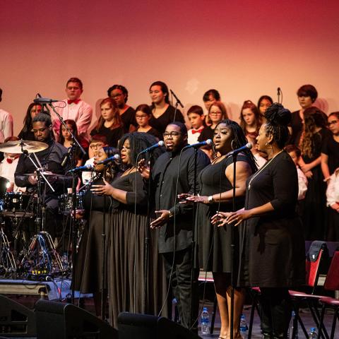 A chorus sings next to a drummer.