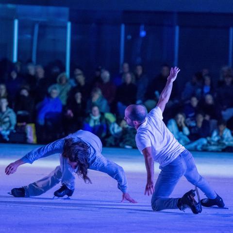 Two male figure skates or ice dancers perform low to the ice.