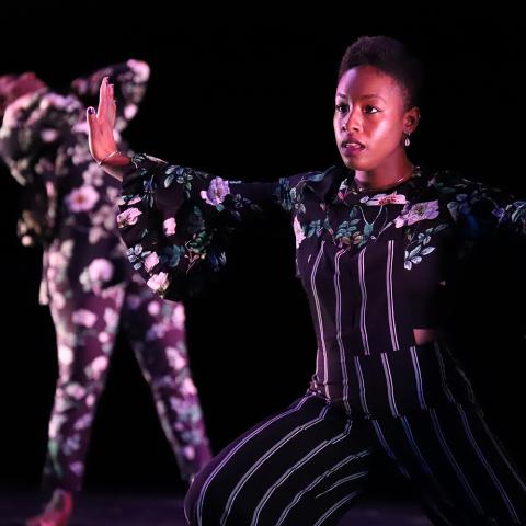 In a spotlight and wearing floral, a dancer spreads her arms wide.