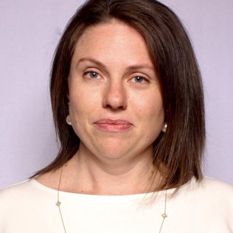 Emily is a white woman with shoulder length brown hair. She wears a white blouse with a boat neck and a necklace.