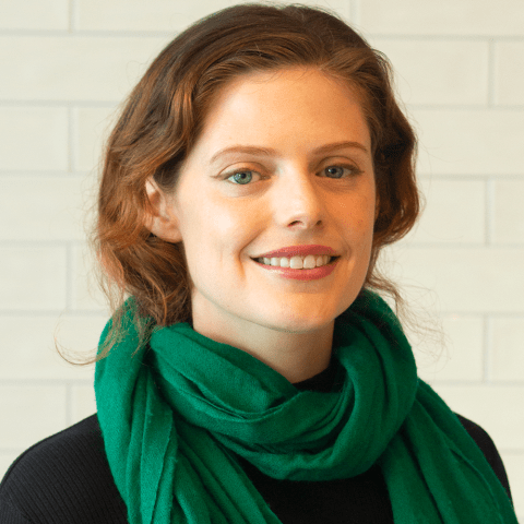 Emm has her auburn hair pulled back. She wears a green scarf that matches her eyes.