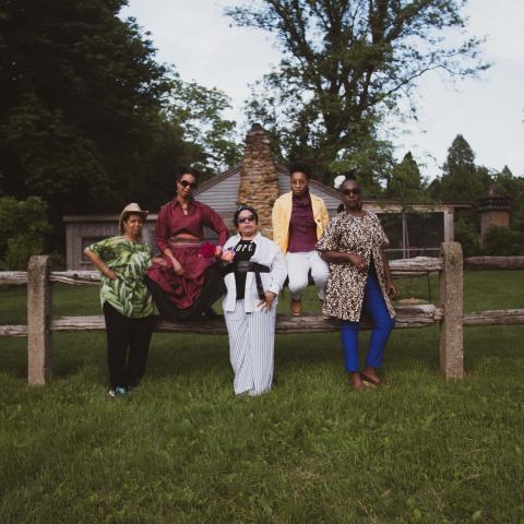 Five black women pose by a log fence.