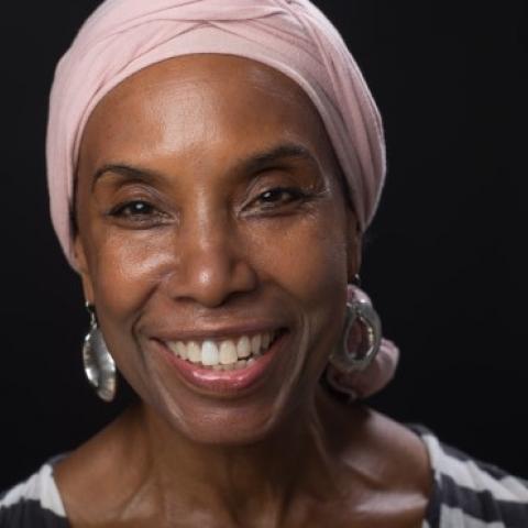 Germaine smiles and wears a light pink headwrap.