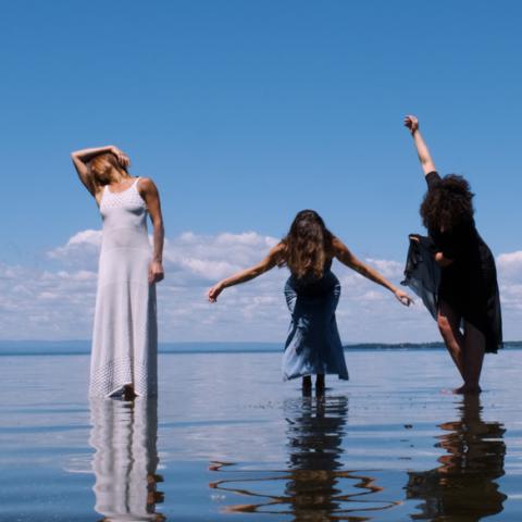 Four femme folks pose on top of shallow water, in dresses.