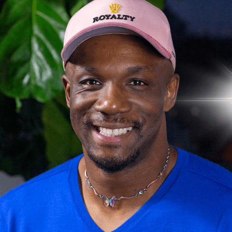 Harold is a Black man, in a colorful choker, indigo sweater, and pink cap with the word "royalty" emblazoned on it.