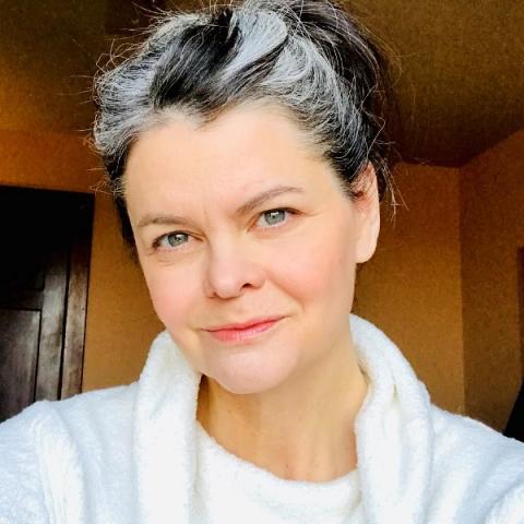 A white woman with dark and silver hair pulled back and wearing a light colored cowl neck sweater
